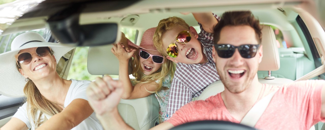 Familie mit zwei Kindern beim Auto fahren in den Sommerurlaub hat Spaß
